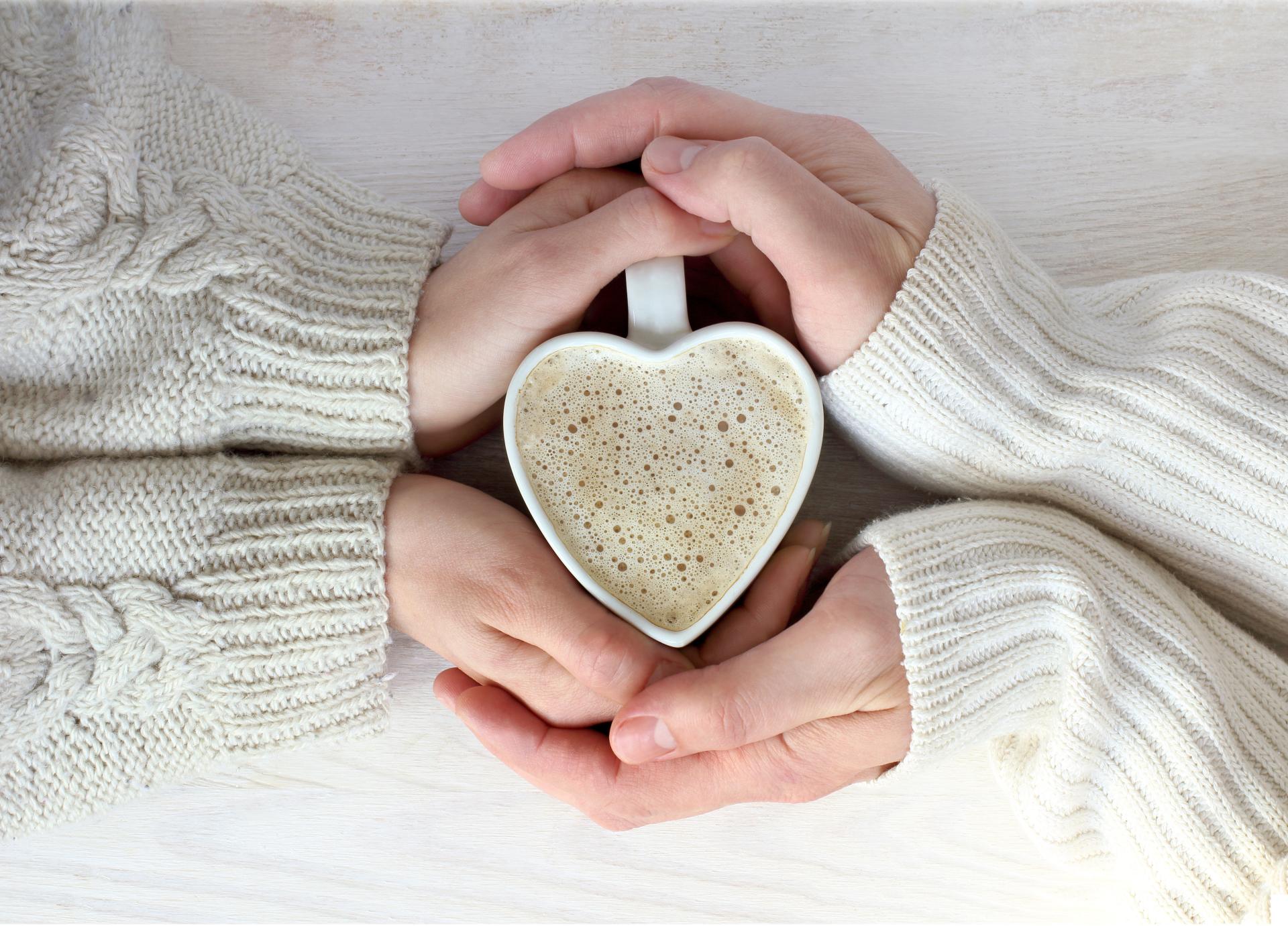 Two hands around a heart shaped mug filled with coffee