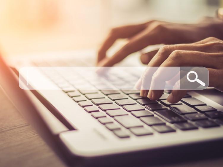 Hands typing on a laptop keyboard with a search bar over the top of the image