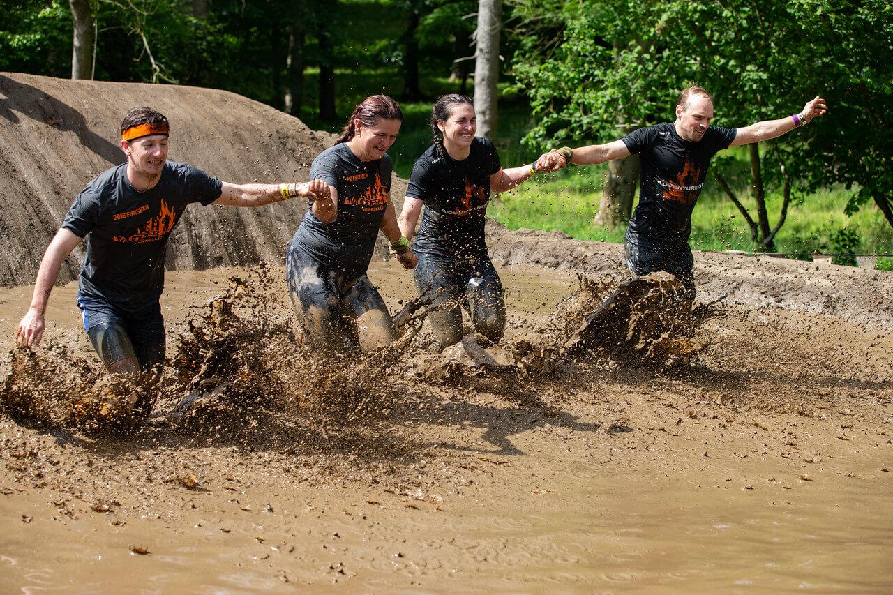Group of four people holding hands splashing through liquid mud