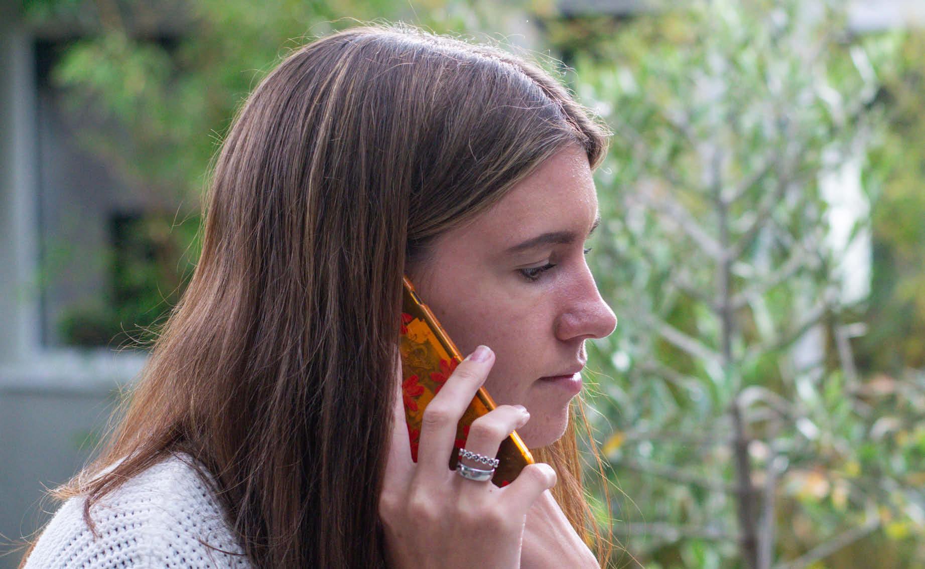 A young woman with long brown hair is on her mobile in the garden