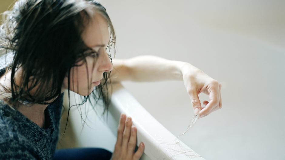 Young woman leaning against a bath with strands of hair in her hand