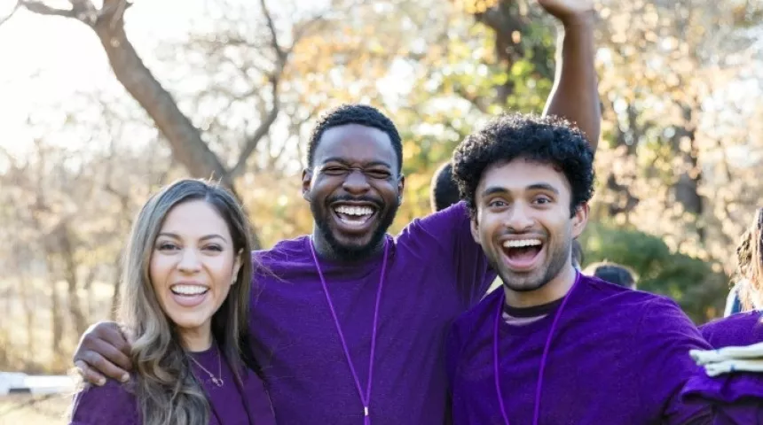 Group photo of volunteers with purple shirts smiling and cheering