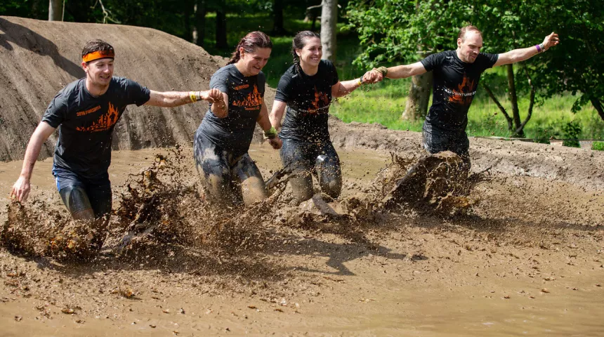 Group of four people holding hands splashing through liquid mud