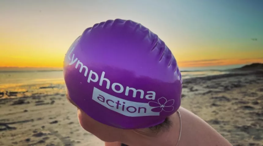 Woman in Lymphoma Action branded swim hat on the beach at sunrise