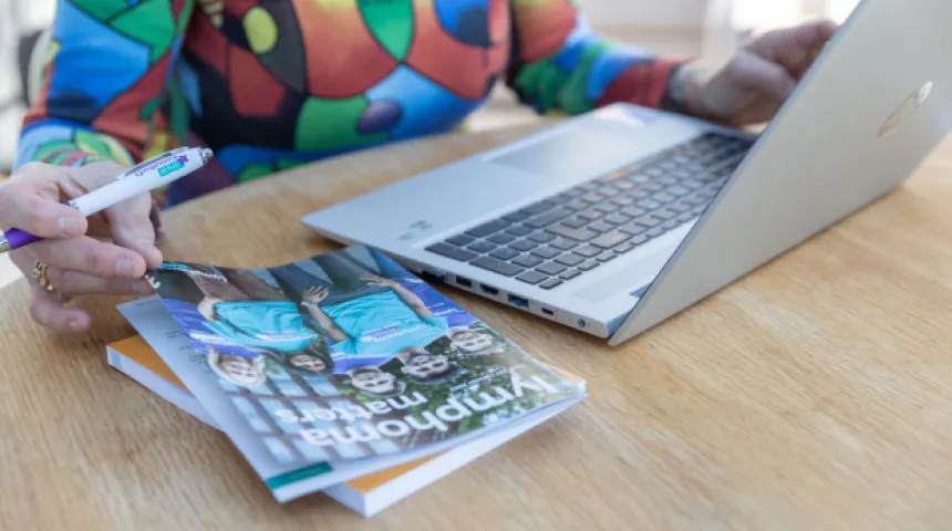 Close up of older woman's hands holding an LA pen as she uses a laptop and looks at an LA magazine