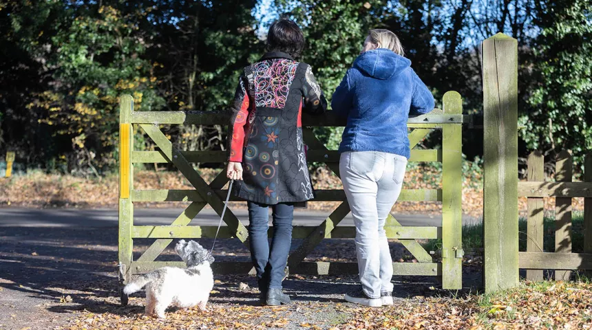 Two ladies leaning on gate, one with a dog on lead
