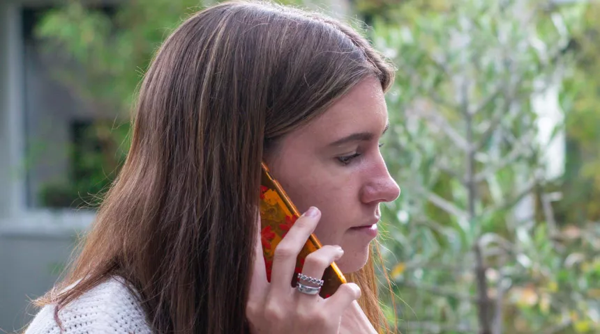 A young woman with long brown hair is on her mobile in the garden