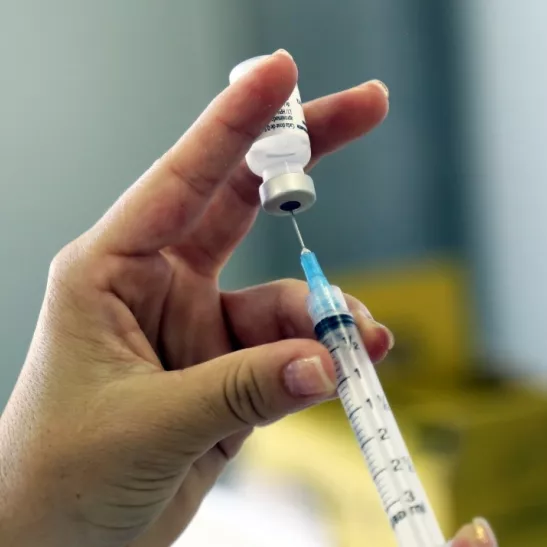 Person using a needle and syringe to draw vaccine from a bottle