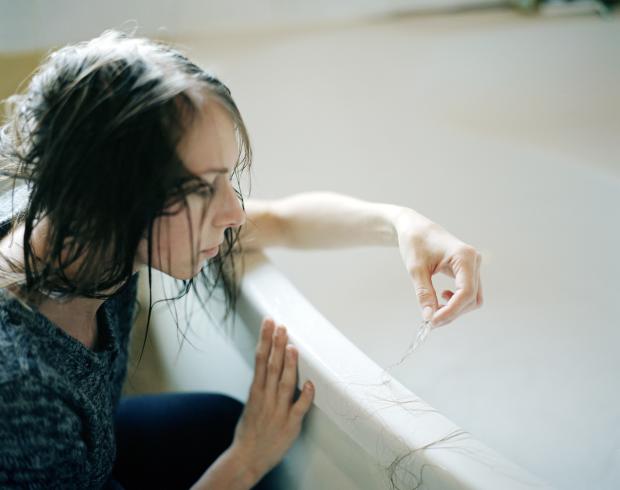 Young woman leaning against a bath with strands of hair in her hand