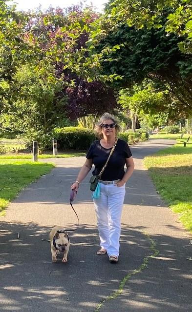 A middle aged woman walking a small dog in a green park