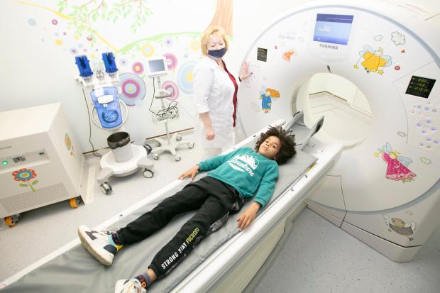 A young mixed race boy lying down ready to go into a PET/CT scanner