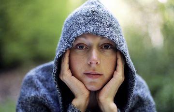 Lady looking at camera with hands on her face and hood up